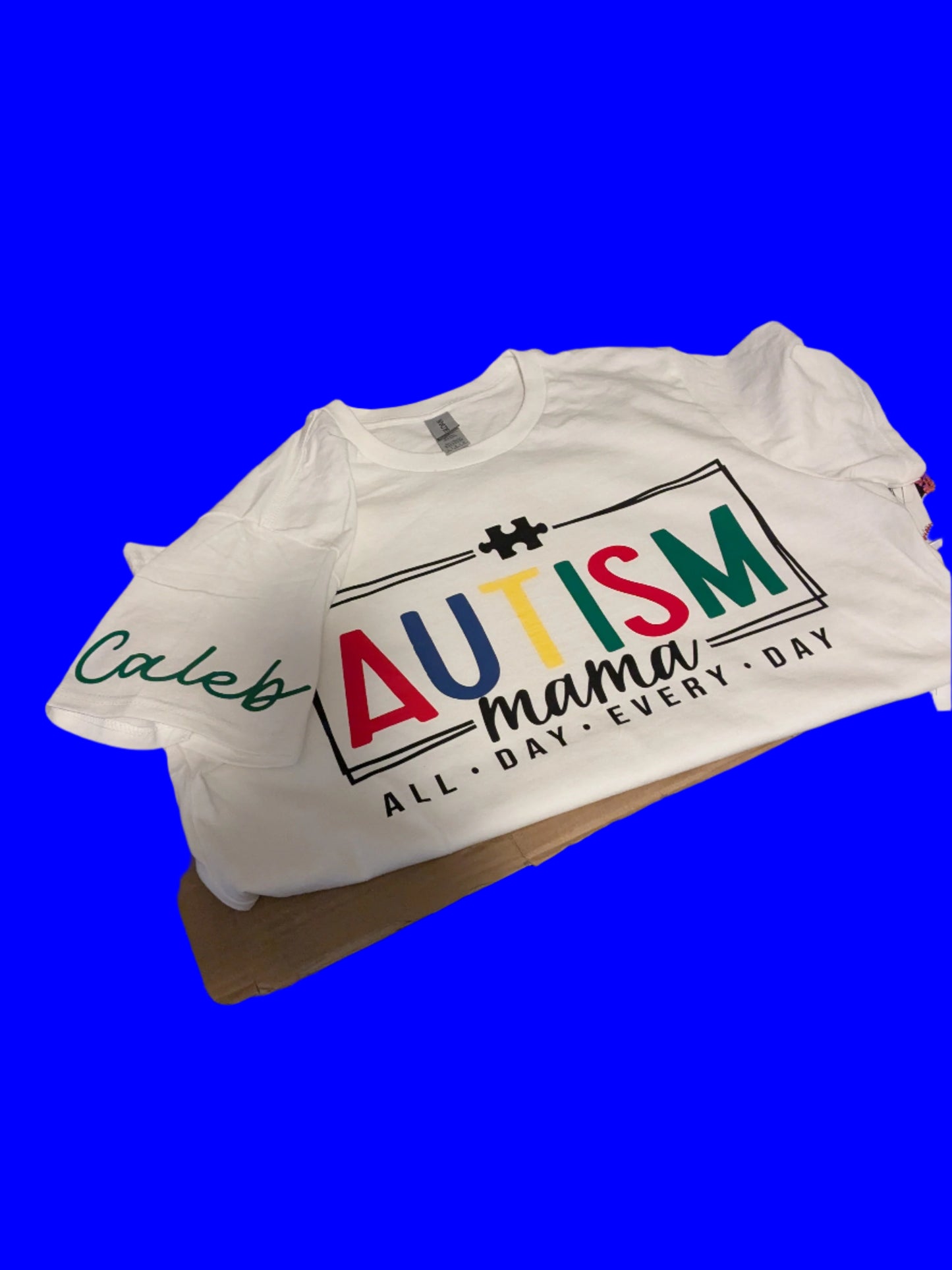 White t-shirt with 'Autism Mama' text on a table against a blue background