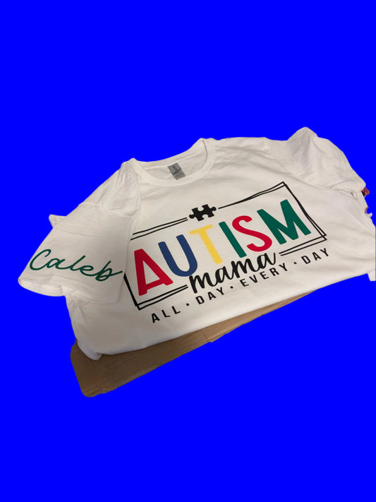 White t-shirt with 'Autism Mama' text on a table against a blue background